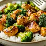 Seared chicken pieces with broccoli on top of white rice in a shallow bowl with black pepper and parsley garnish