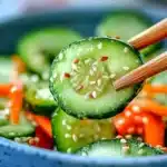 Wooden chopsticks holding cucumber slice from Asian salad