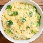 Close-up of creamy cheesy broccoli rice in white bowl showing melted cheese coating rice and bright green broccoli