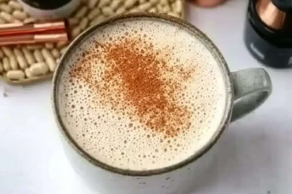 A cinnamon-topped creamy coffee with supplements in the background, perfect for a wellness-focused morning.