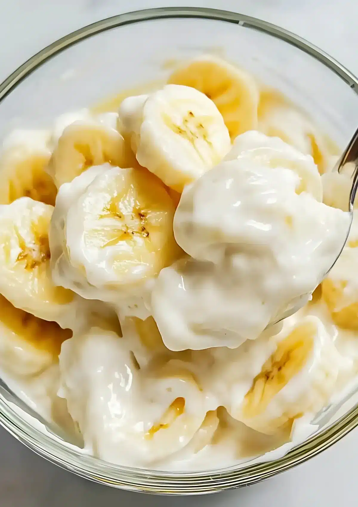 Close-up of creamy banana salad with fresh banana slices and mayonnaise in a glass bowl

