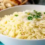 Finished creamy orzo side dish in white serving bowl topped with grated Parmesan cheese and fresh parsley
