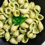 Creamy pesto pasta with shell pasta in a black skillet, garnished with fresh basil leaves and coated in vibrant green pesto sauce