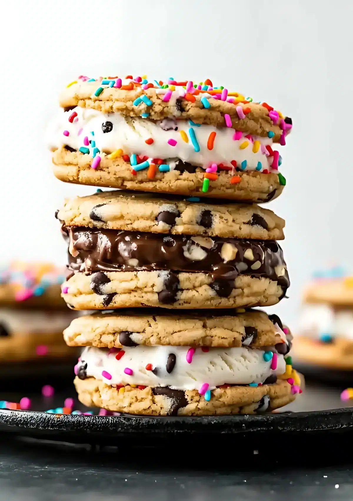 Tall stack of festive cookie ice cream sandwiches with colorful sprinkles, chocolate drizzle, and various toppings