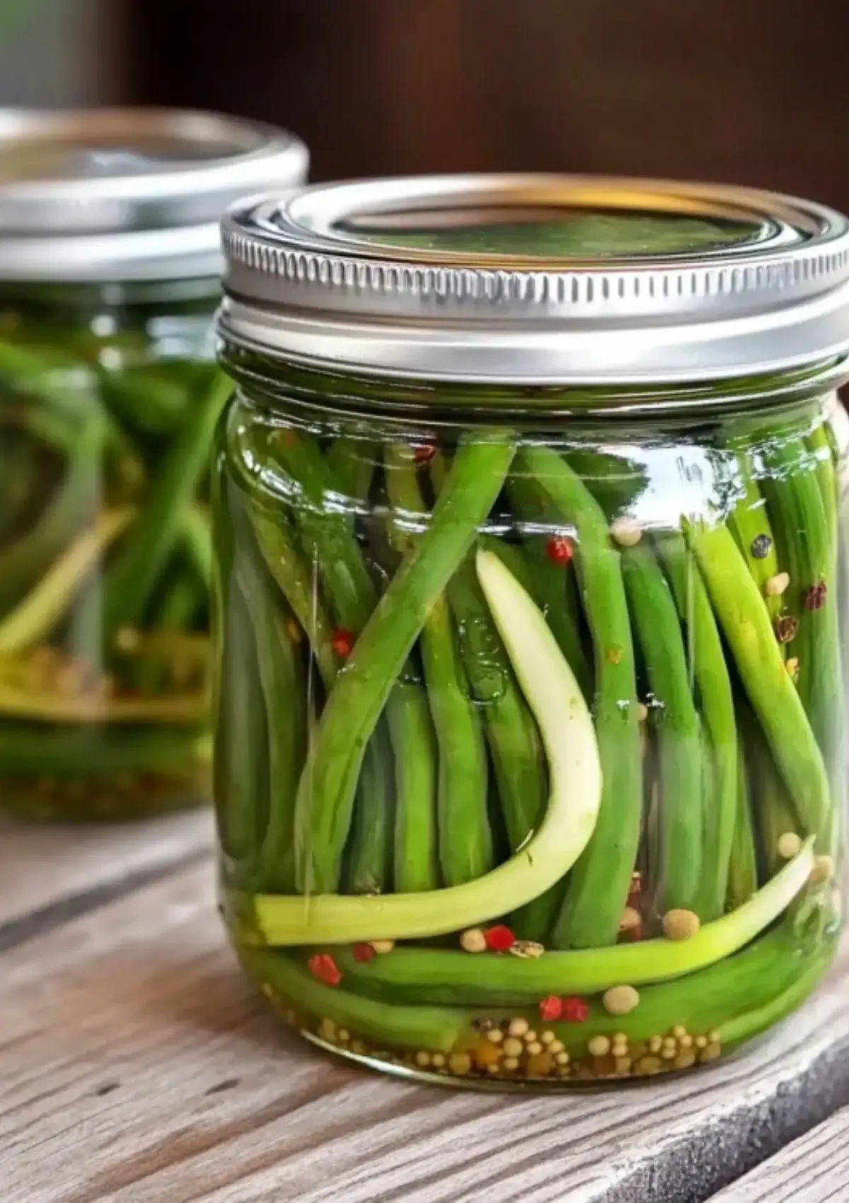 Pickled garlic scapes in mason jars with spices and clear brine on wooden surface