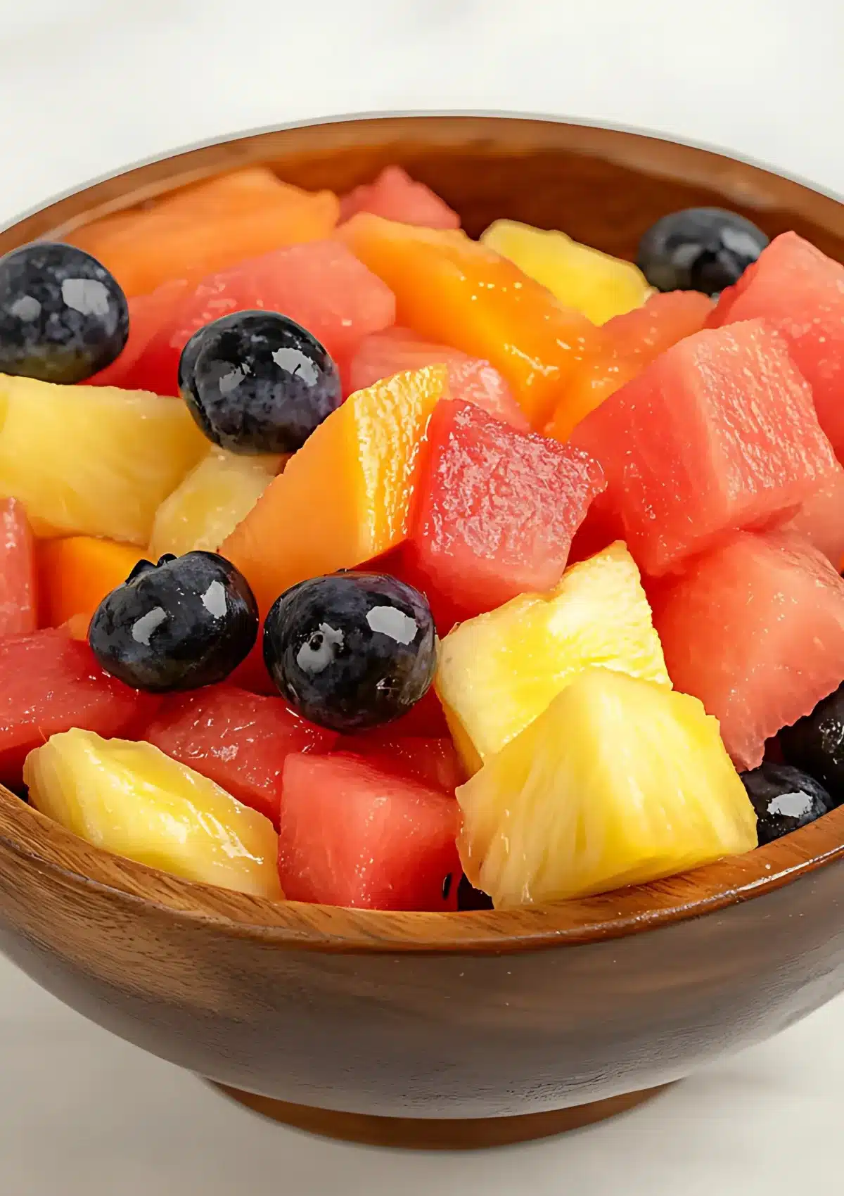 Colorful easy tropical fruit salad served in rustic wooden bowl showing natural fruit juices