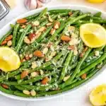 Elegant presentation of green beans almondine garnished with lemon wedges and parmesan in white oval dish