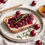 Roasted cherries on cream cheese toast garnished with fresh thyme and honey drizzle