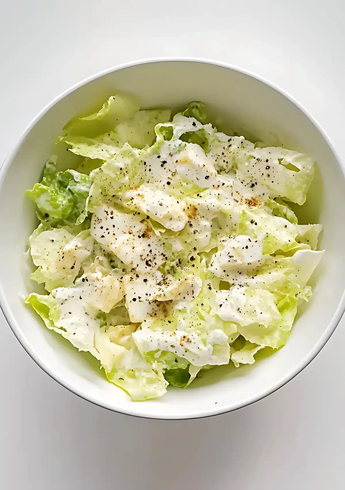 Overhead view of completed Swedish pizza salad in white bowl with lettuce fully coated in speckled creamy dressing