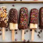 Chocolate covered bananas with colorful sprinkles and toppings on parchment lined baking sheet