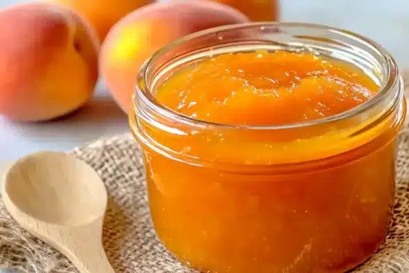 Glass jar of golden apricot preserved with wooden spoon and fresh apricots on burlap cloth