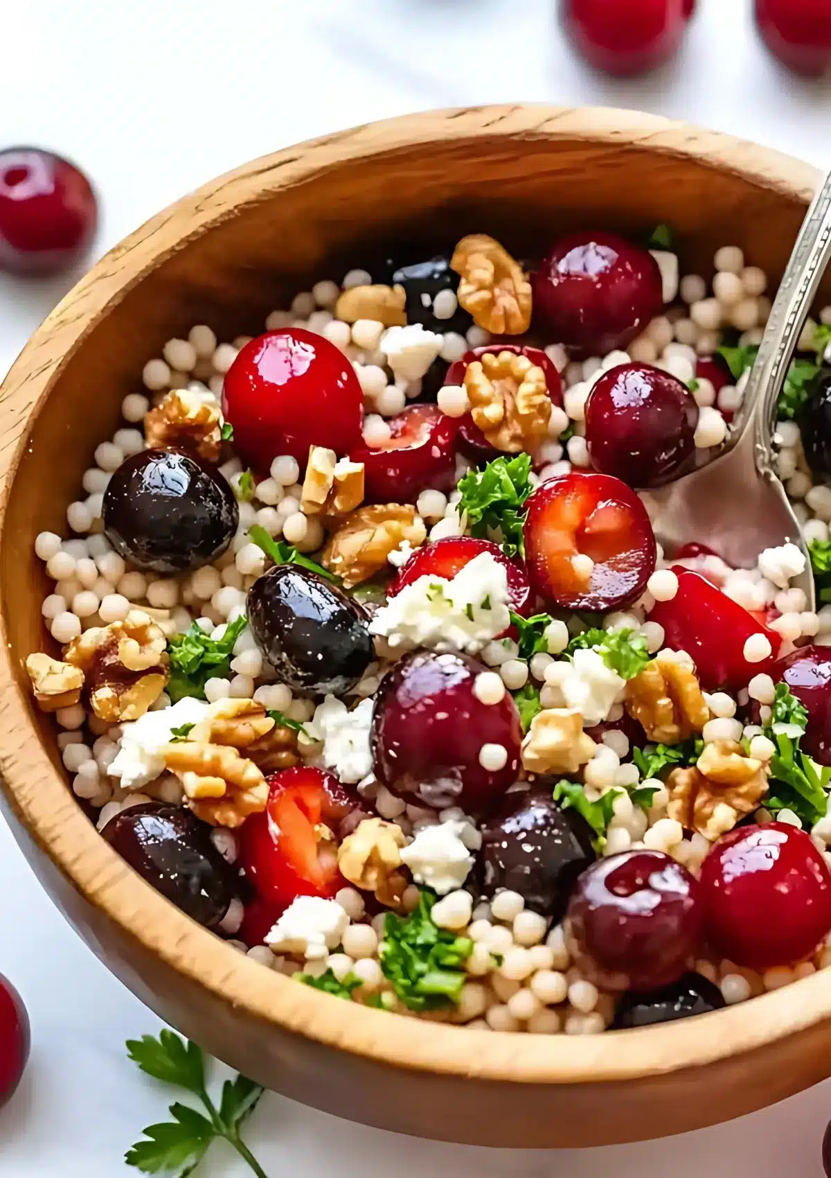 Cherry Walnut Couscous Salad in wooden bowl with serving spoon showing fresh cherries, crumbled feta and chopped walnuts