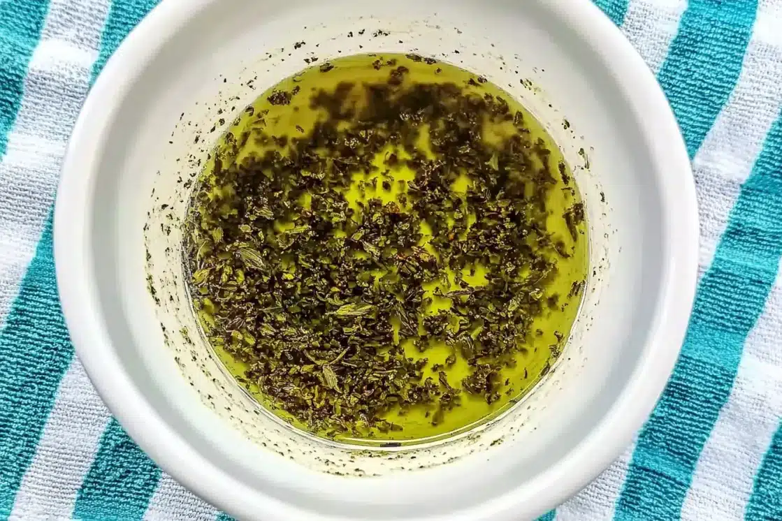 Herb oil marinade with oregano, basil and garlic in white bowl on striped kitchen towel