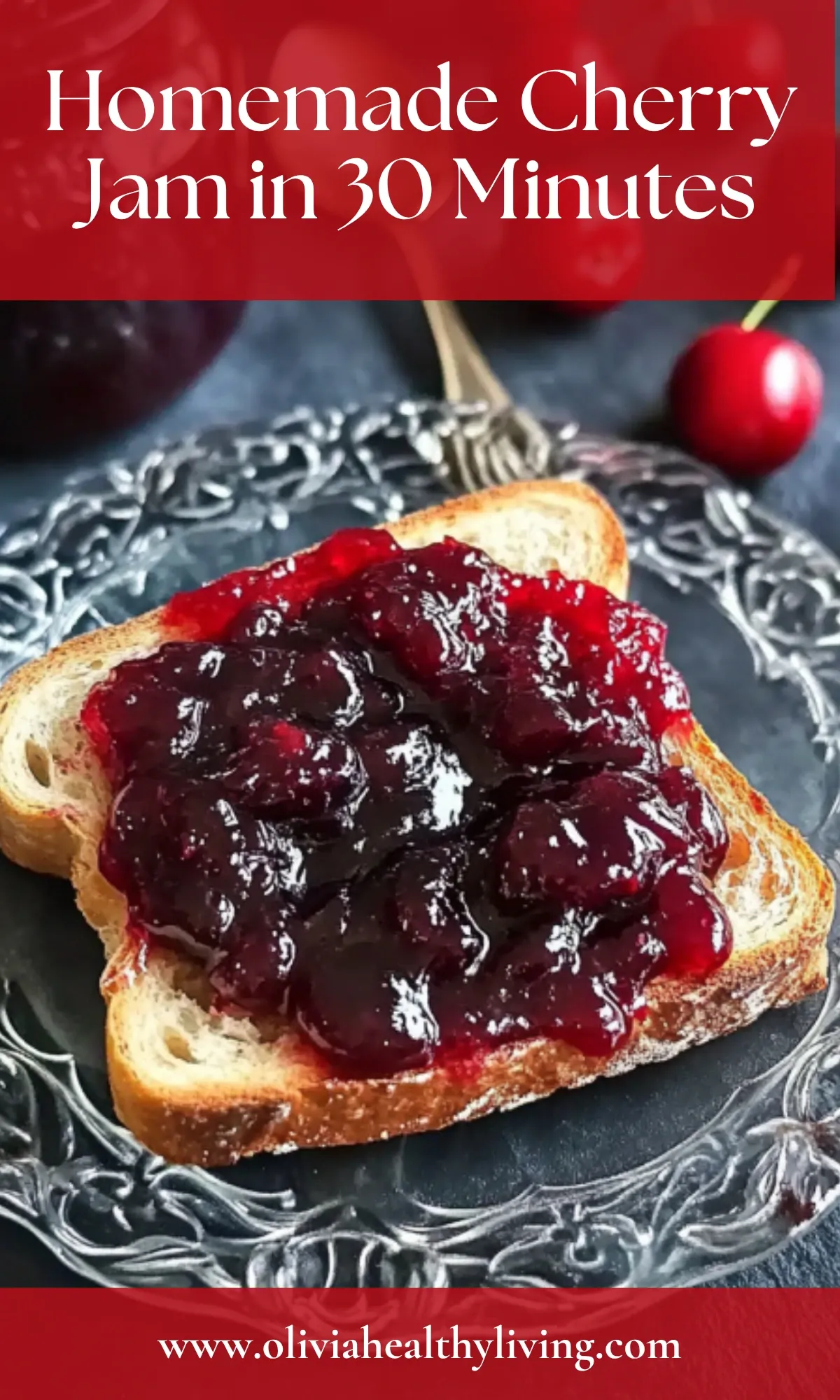 Slice of bread topped with homemade cherry jam on dark plate with fresh cherries and gold spoon nearby