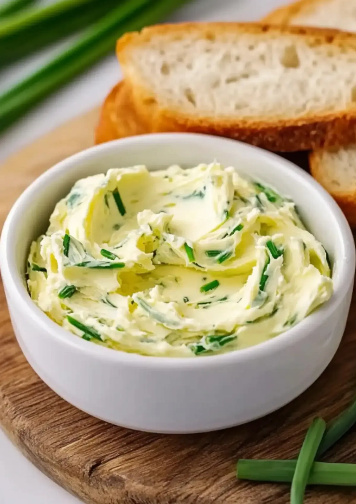 Close-up of garlic scapes butter in white ceramic bowl on wooden board with fresh bread and green scapes