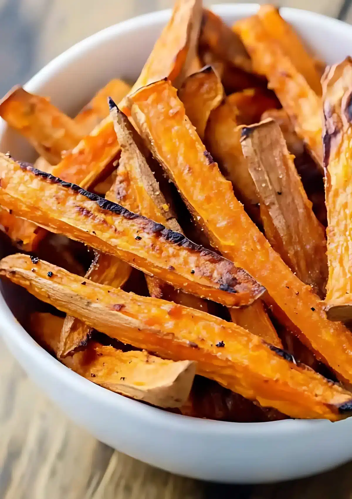 Close-up of crispy sweet potato fries in a white bowl, showing golden-brown edges and perfect texture with visible seasoning