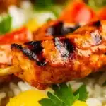 Close-up of grilled Turkish chicken Adana kebab skewer with char marks, served on saffron rice with parsley and tomato