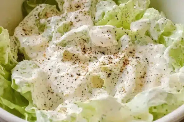 Close-up of iceberg lettuce leaves coated in creamy white dressing with visible black pepper specks throughout