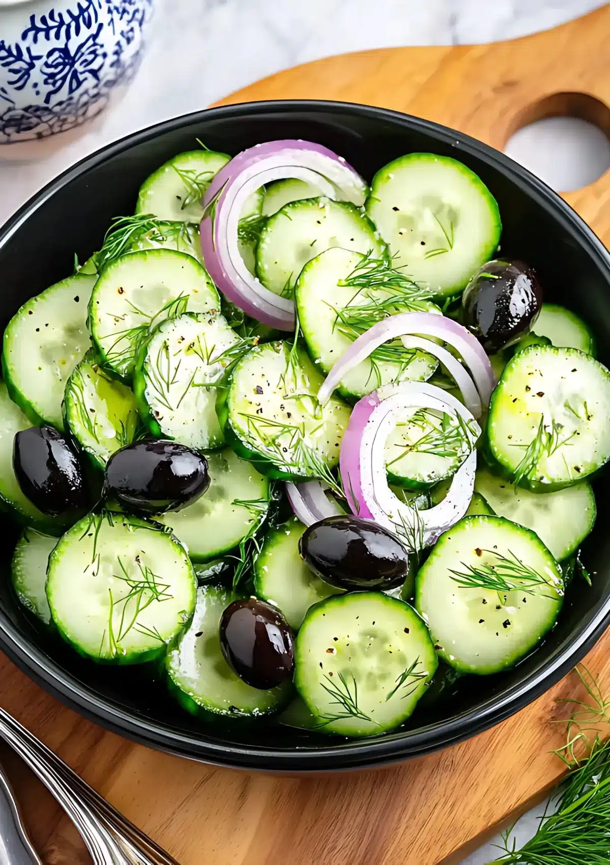 Close-up view of keto cucumber salad showing fresh dill, sliced cucumbers, black olives and red onion in black serving bowl