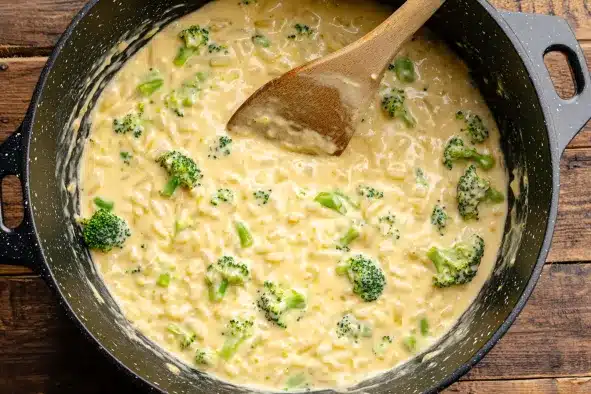 Combining cooked rice with creamy cheese sauce and broccoli florets in skillet to make cheesy broccoli rice