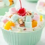 Colorful ambrosia salad served in mint green fluted bowls, topped with maraschino cherries, pastel marshmallows, chopped pecans, and mandarin oranges