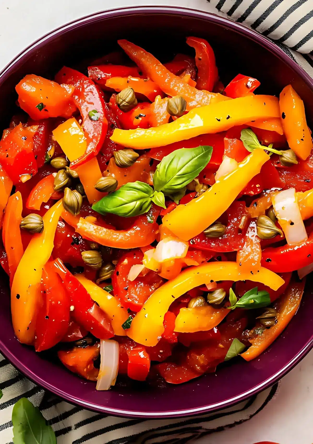 Close-up of traditional pepperonata with caramelized bell peppers, capers, and fresh basil in a burgundy skillet