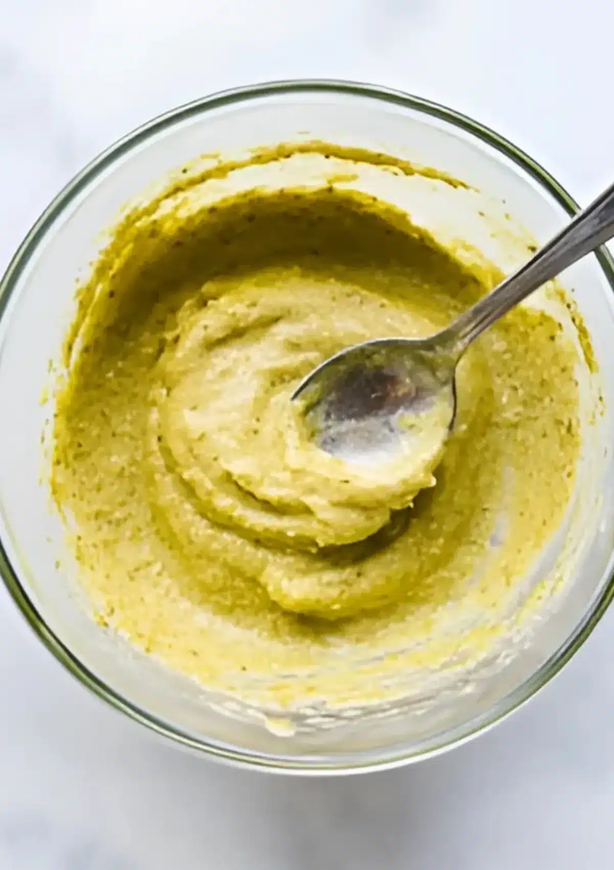 Bowl of homemade pistachio frangipane cream with a spoon, ready to be spread inside croissants.

