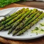 Grilled asparagus spears on white plate with fork, herb garnish and melted butter sauce