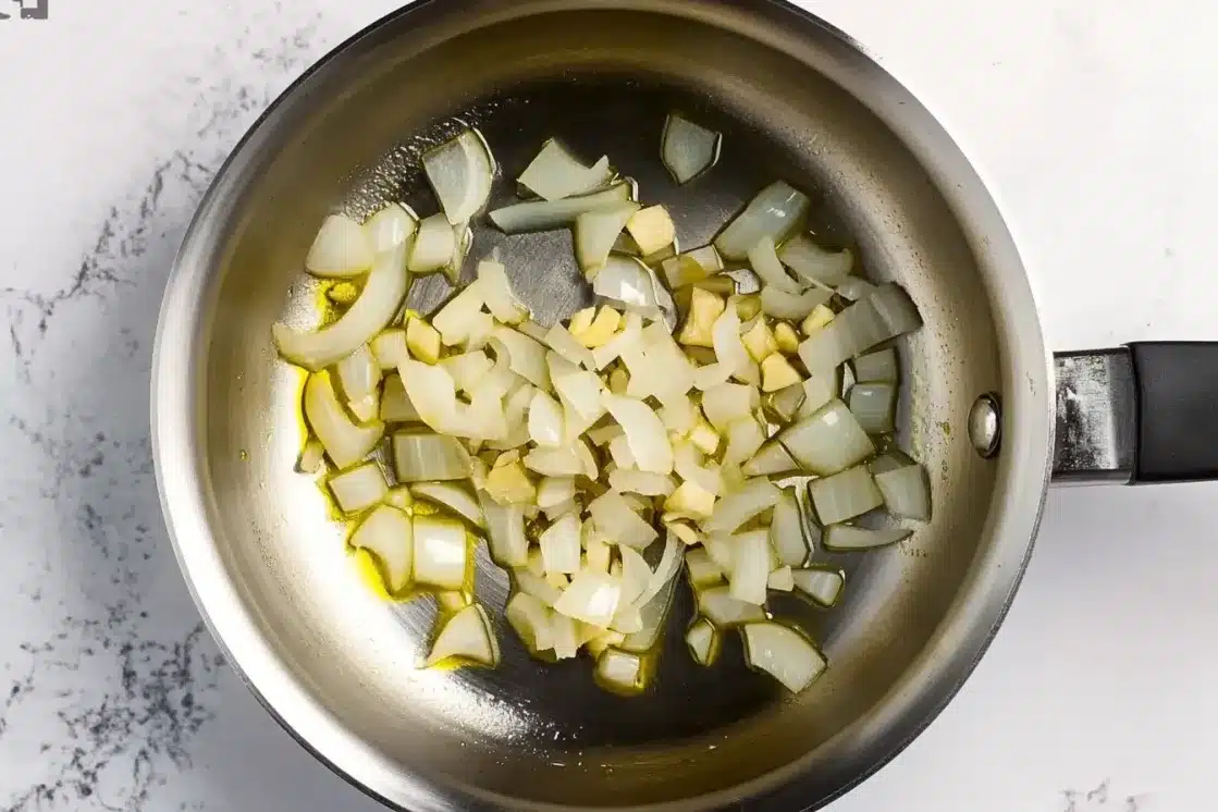 Diced white onions cooking in stainless steel pan with vegan butter for creamed spinach base
