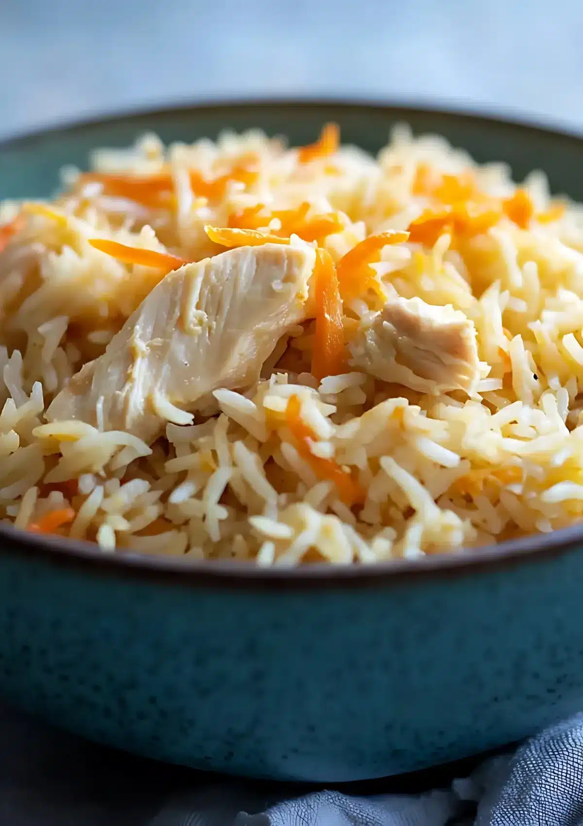 Juicy pieces of chicken breast on top of basmati rice and carrots in a teal ceramic bowl.

