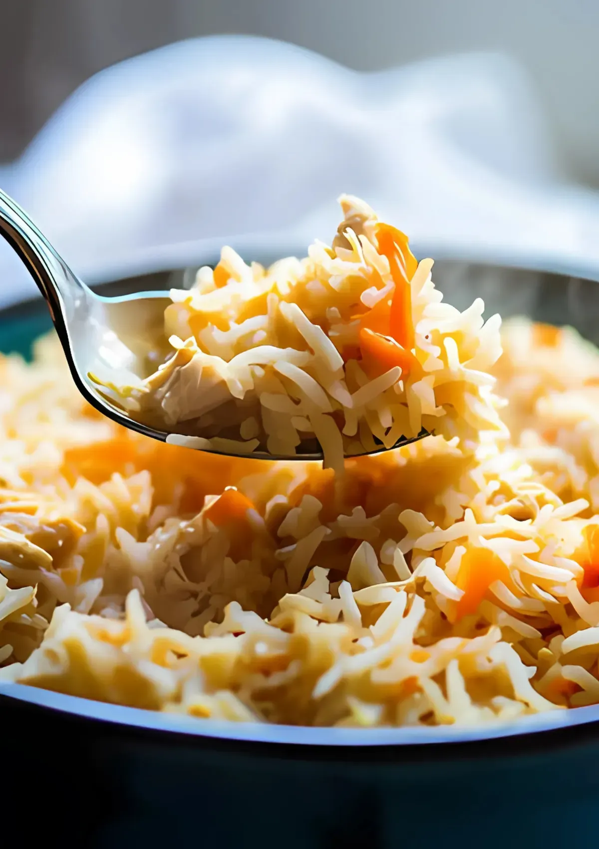 A spoonful of fluffy rice and carrots being lifted from a teal bowl, showing texture and color contrast.

