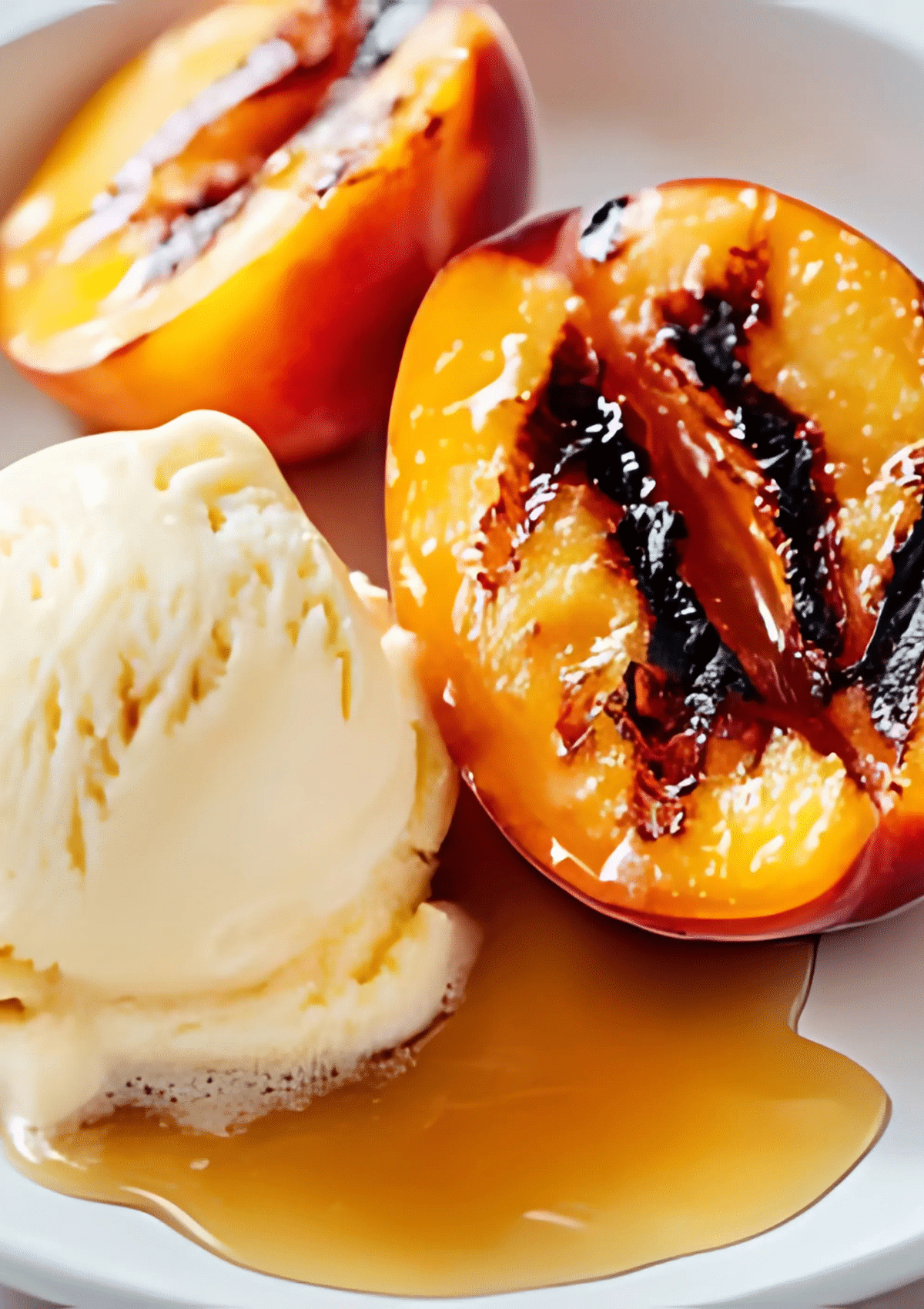 Two grilled peach halves with charred grill lines, paired with vanilla ice cream and brown sugar syrup on a white plate.