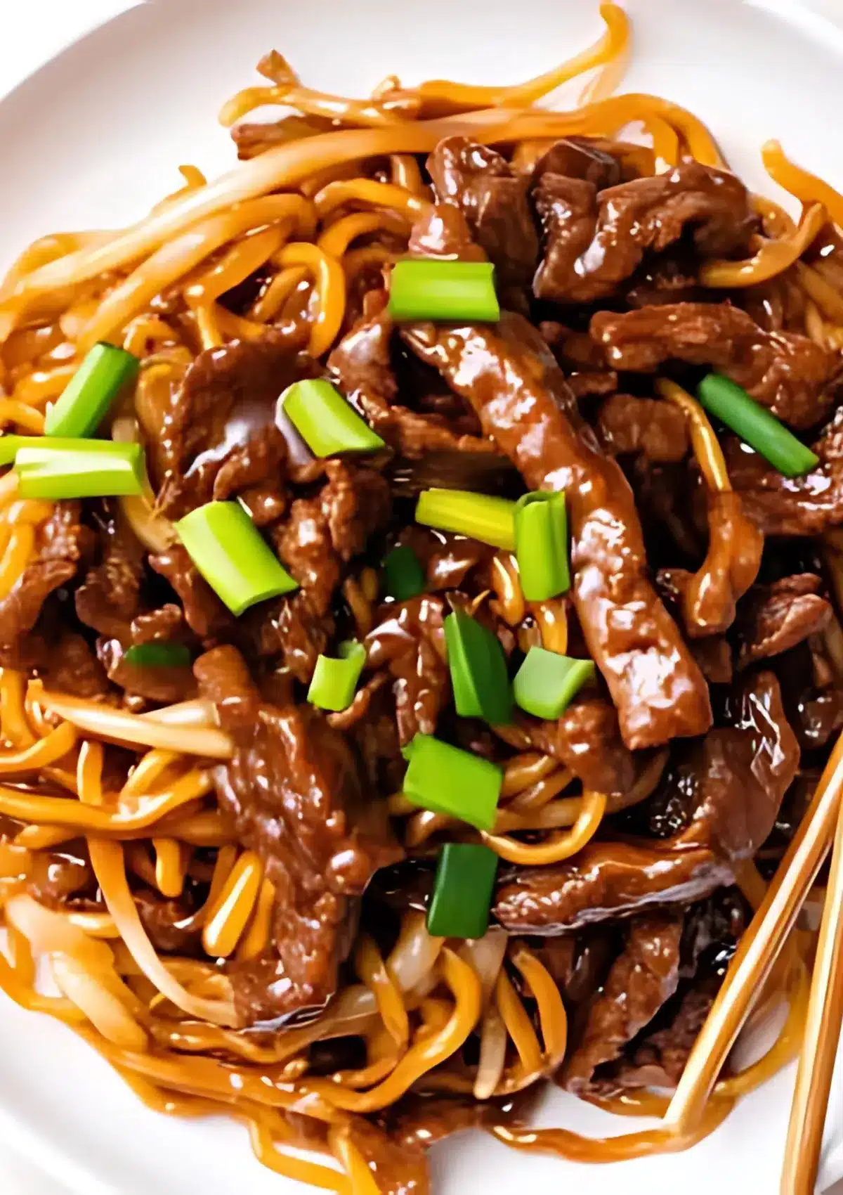 Flat-lay of Mongolian beef noodles in a white bowl, featuring stir-fried beef strips, thick noodles, and vibrant chopped green onions.

