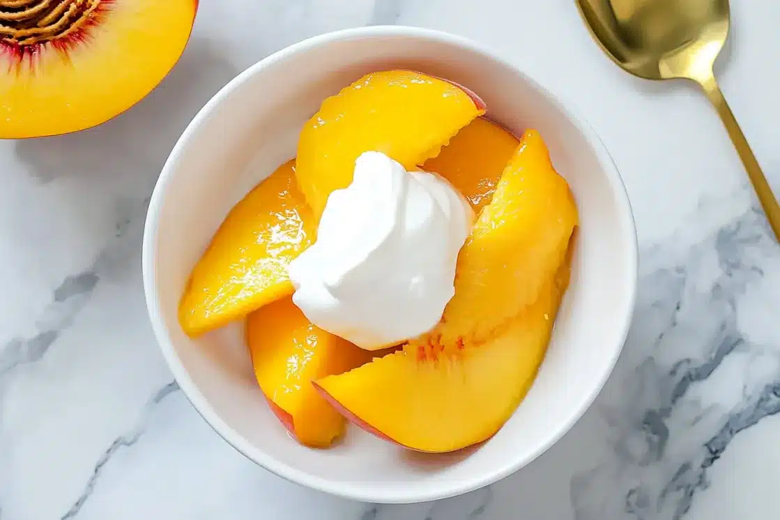 Fresh peaches in syrup served in white bowl with whipped cream and fresh peach half