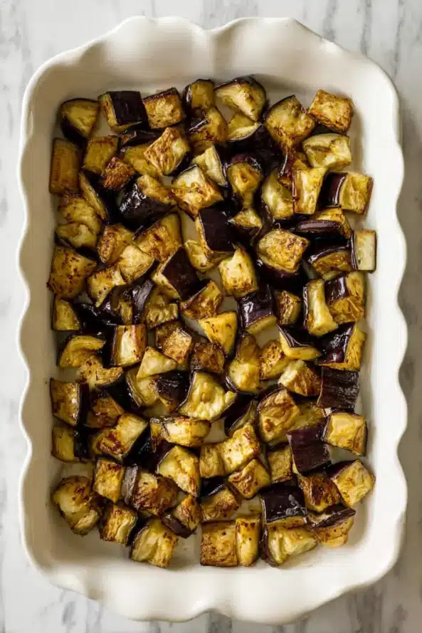 Layered eggplant moussaka in a ceramic dish showing caramelized onions, chickpeas, and chunky tomato sauce, ready for baking.

