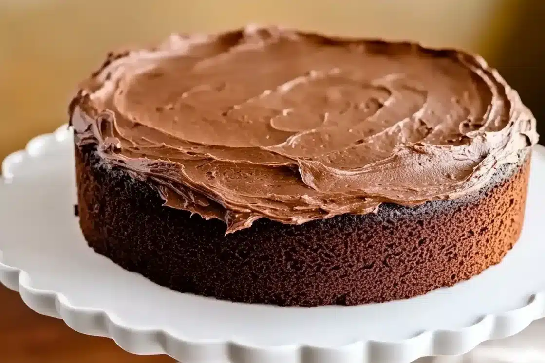 Complete chocolate layer cake with smooth chocolate frosting on white pedestal cake stand