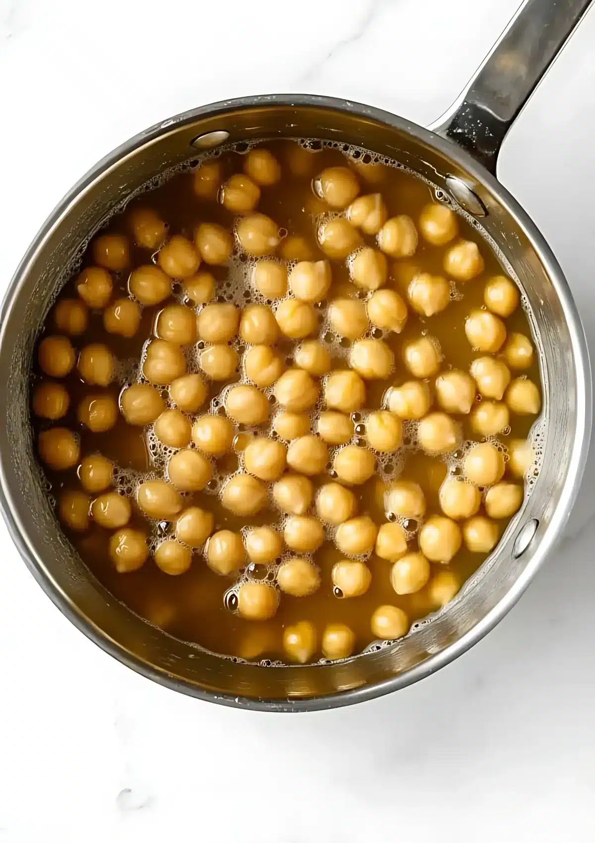 Chickpeas simmering in a pot of water on a white marble countertop.