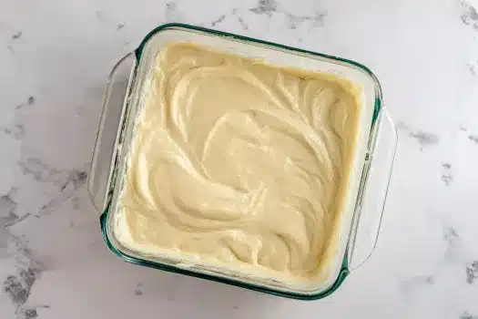 A square glass dish filled with smooth vanilla cake batter, ready to be baked.

