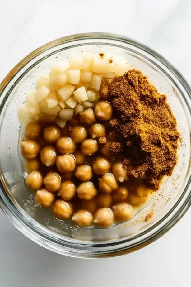 Bowl of chickpeas, minced garlic, and ground spices with liquid, ready for mashing.