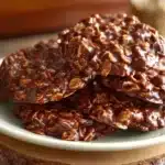 Close-up of chocolate no bake cookies stacked on a white plate atop a rustic wooden pedestal.