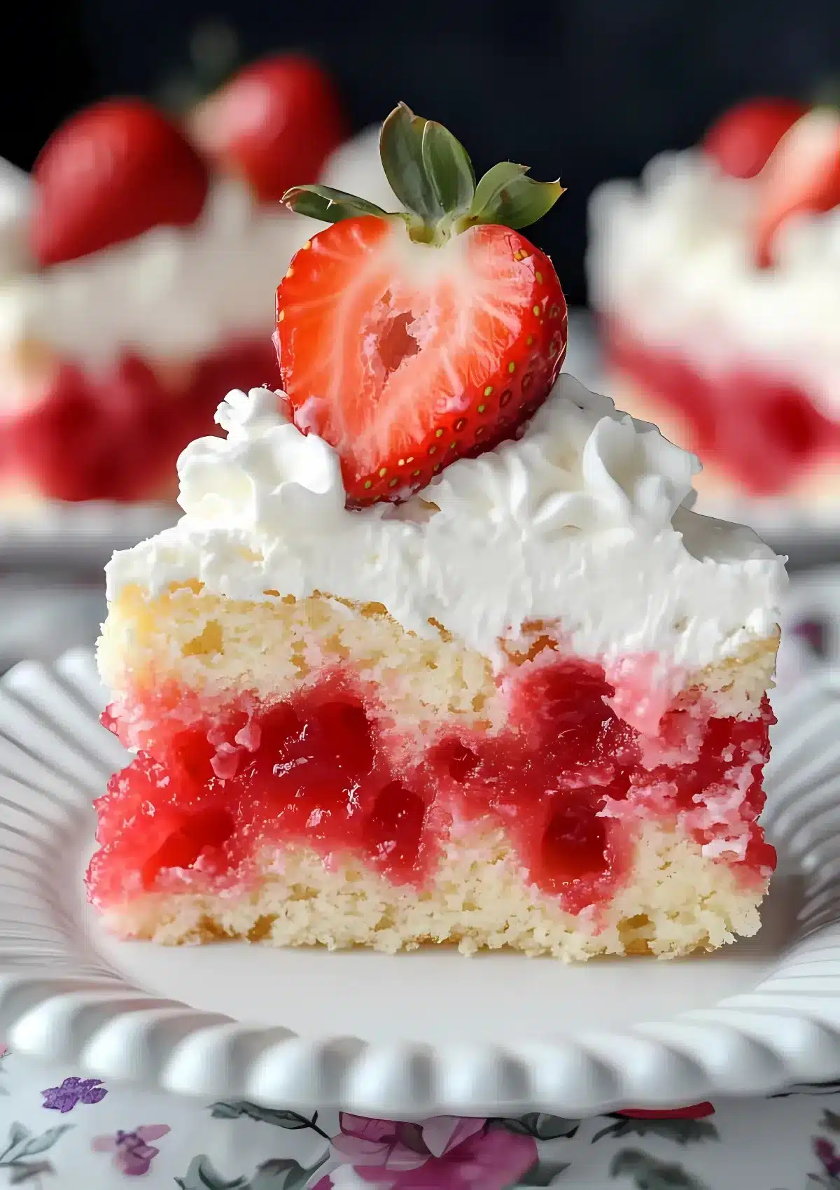 A slice of strawberry poke cake with whipped cream and a halved strawberry on top.