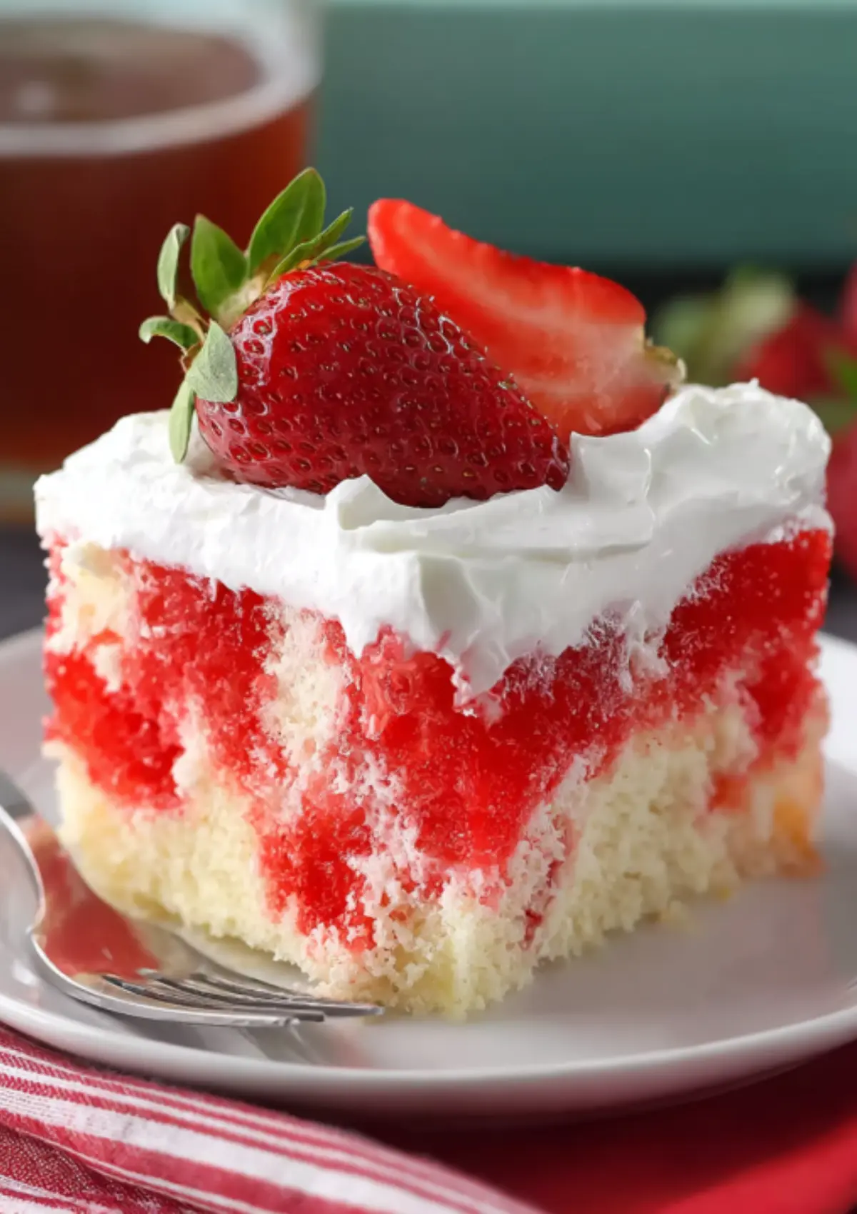 Close-up of strawberry cake slice with white frosting and fresh strawberry garnish on white plate with red striped napkin