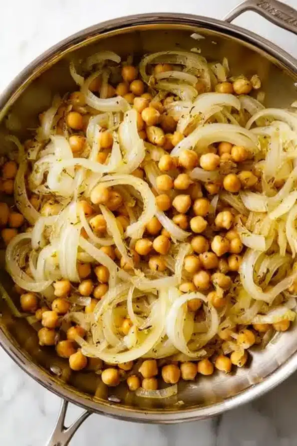  A sauté pan with cooked onions, fresh tomatoes, chickpeas, and herbs beginning to form the sauce for eggplant moussaka.