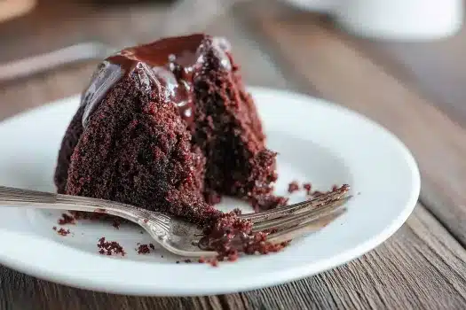 Slice of moist chocolate Bundt cake on a white plate with a silver fork and rich chocolate glaze dripping

