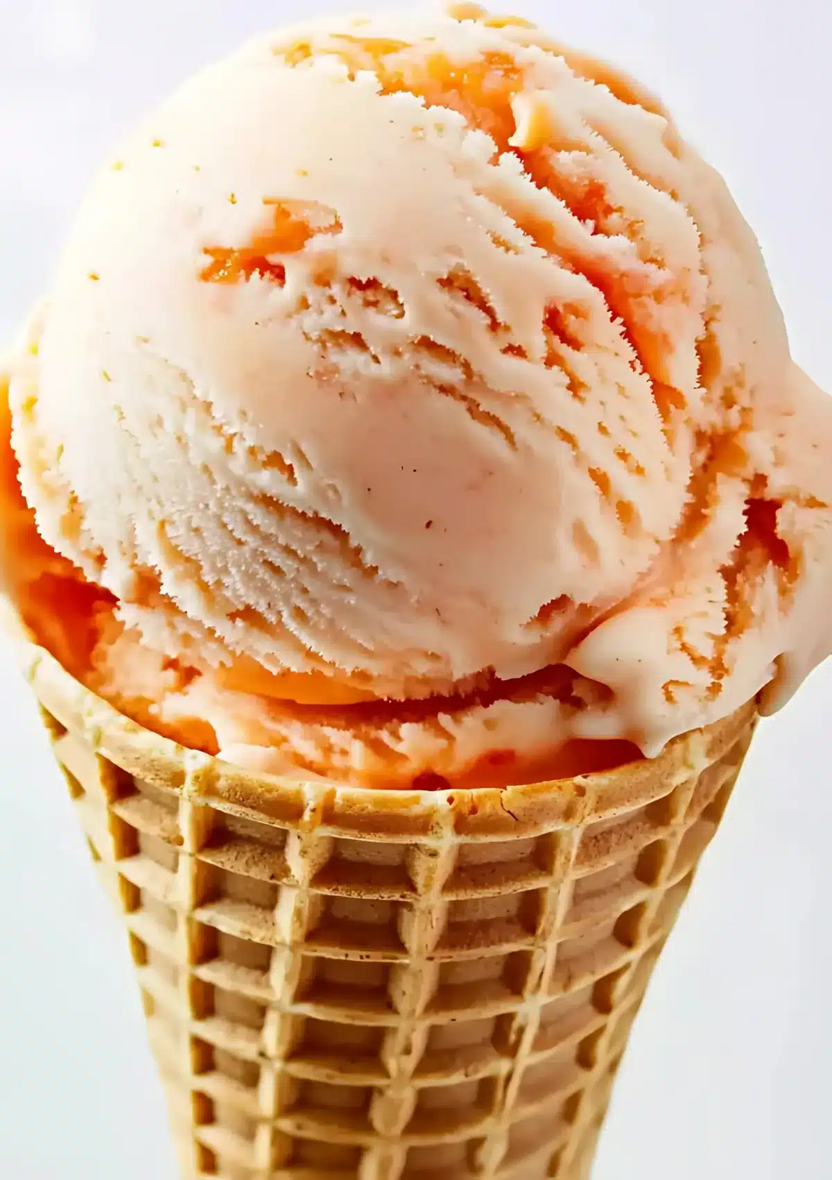 Close-up of peach ice cream scoop in waffle cone showing creamy texture with orange peach swirls
