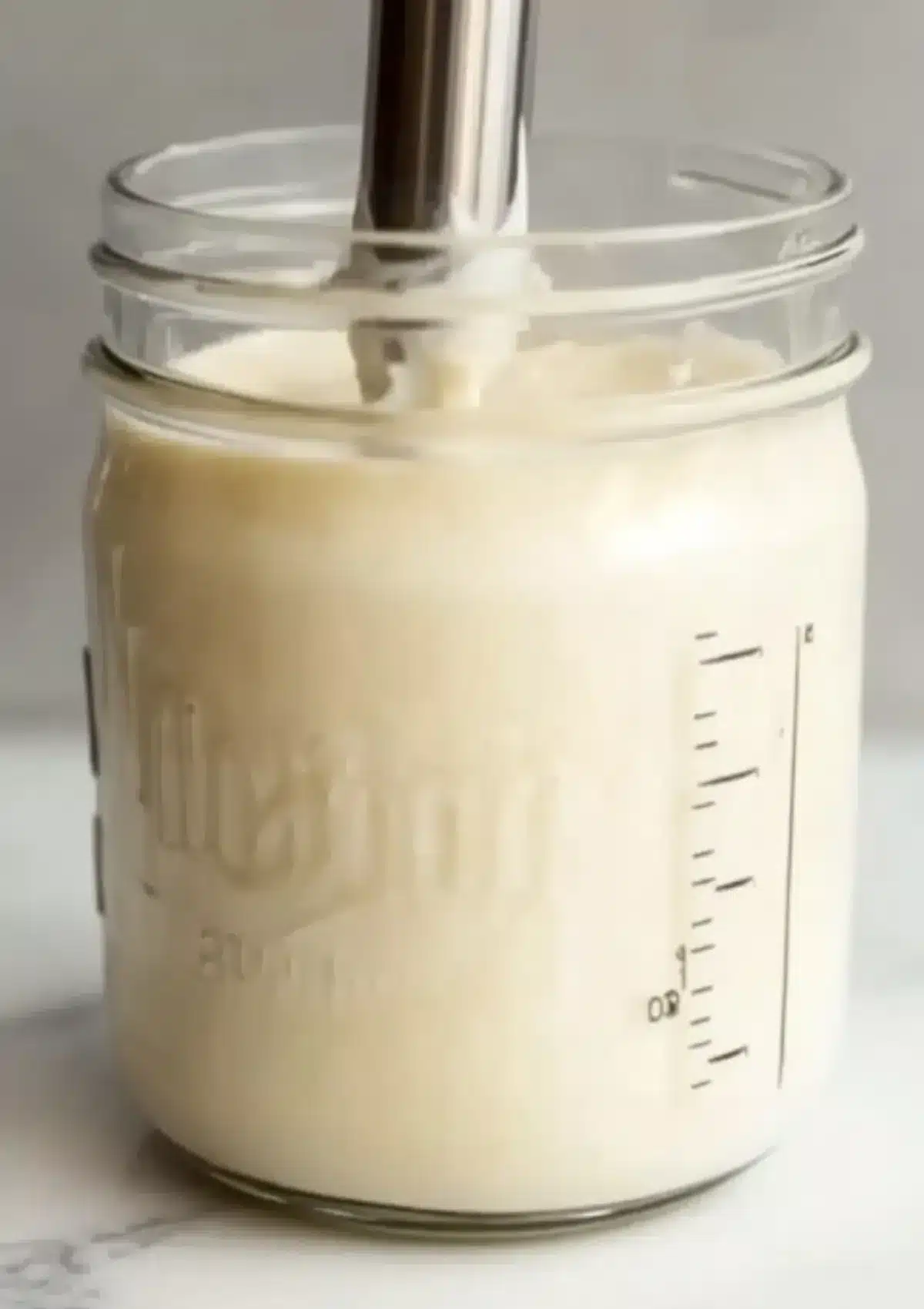 Jar filled with creamy Lebanese garlic sauce during immersion blending process