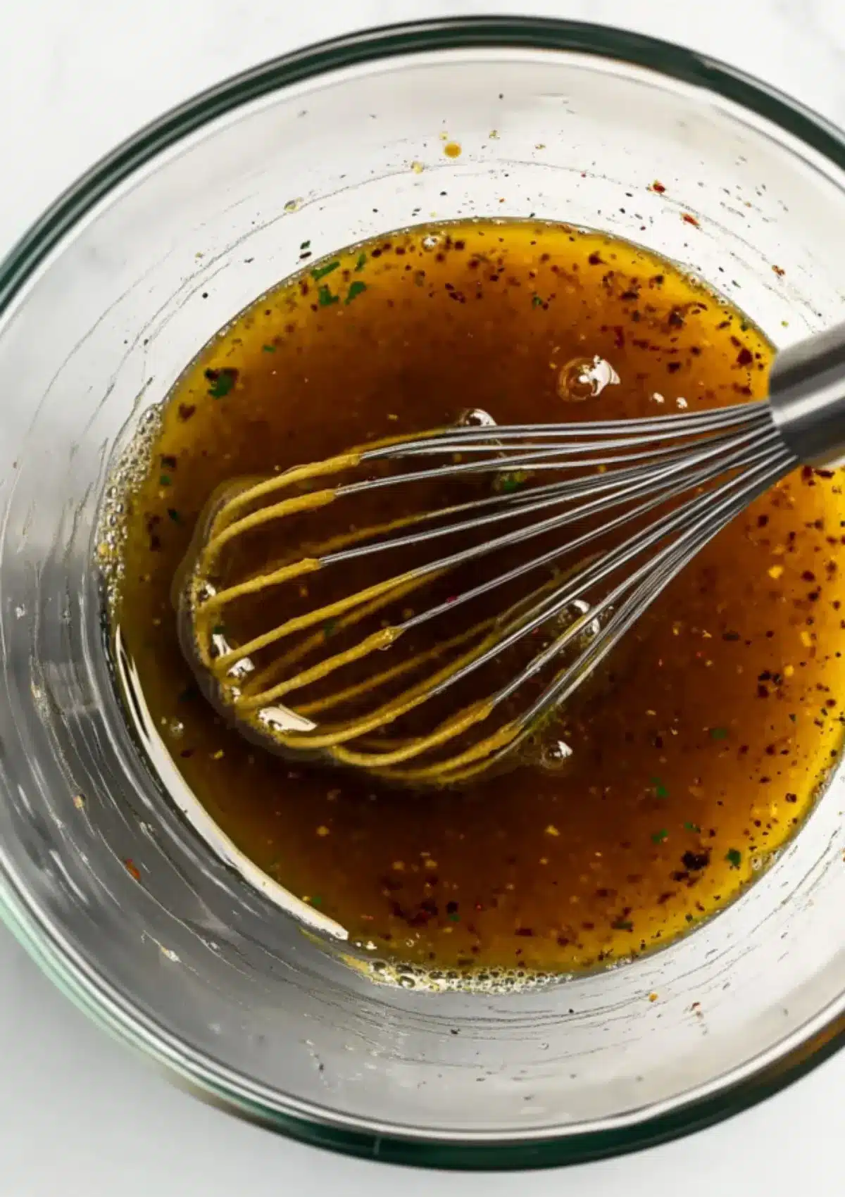 Pomegranate molasses vinaigrette with sumac and herbs being whisked in a clear bowl for fattoush salad