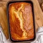 Baked Southern peach bread in dark loaf pan with golden brown top and crack down center, butter dish nearby