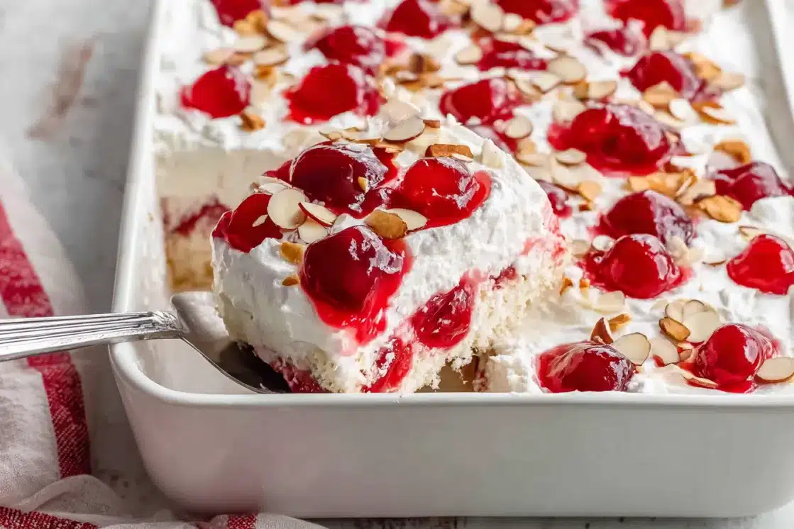 Heaven on Earth Cake in white baking dish being served with spoon showing cherry pie filling and whipped topping layers
