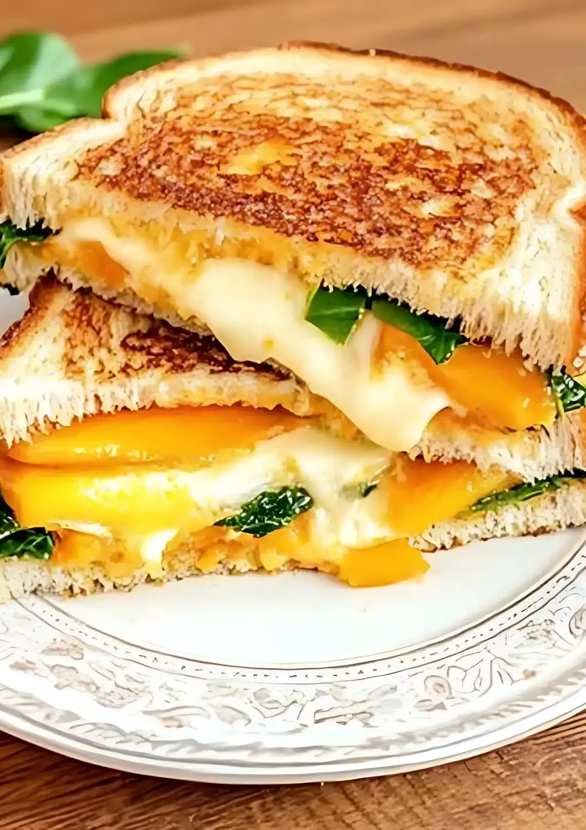 Close-up of grilled cheese sandwich with peaches cut in half showing melted cheese stretching between the layers with spinach and peach slices visible
